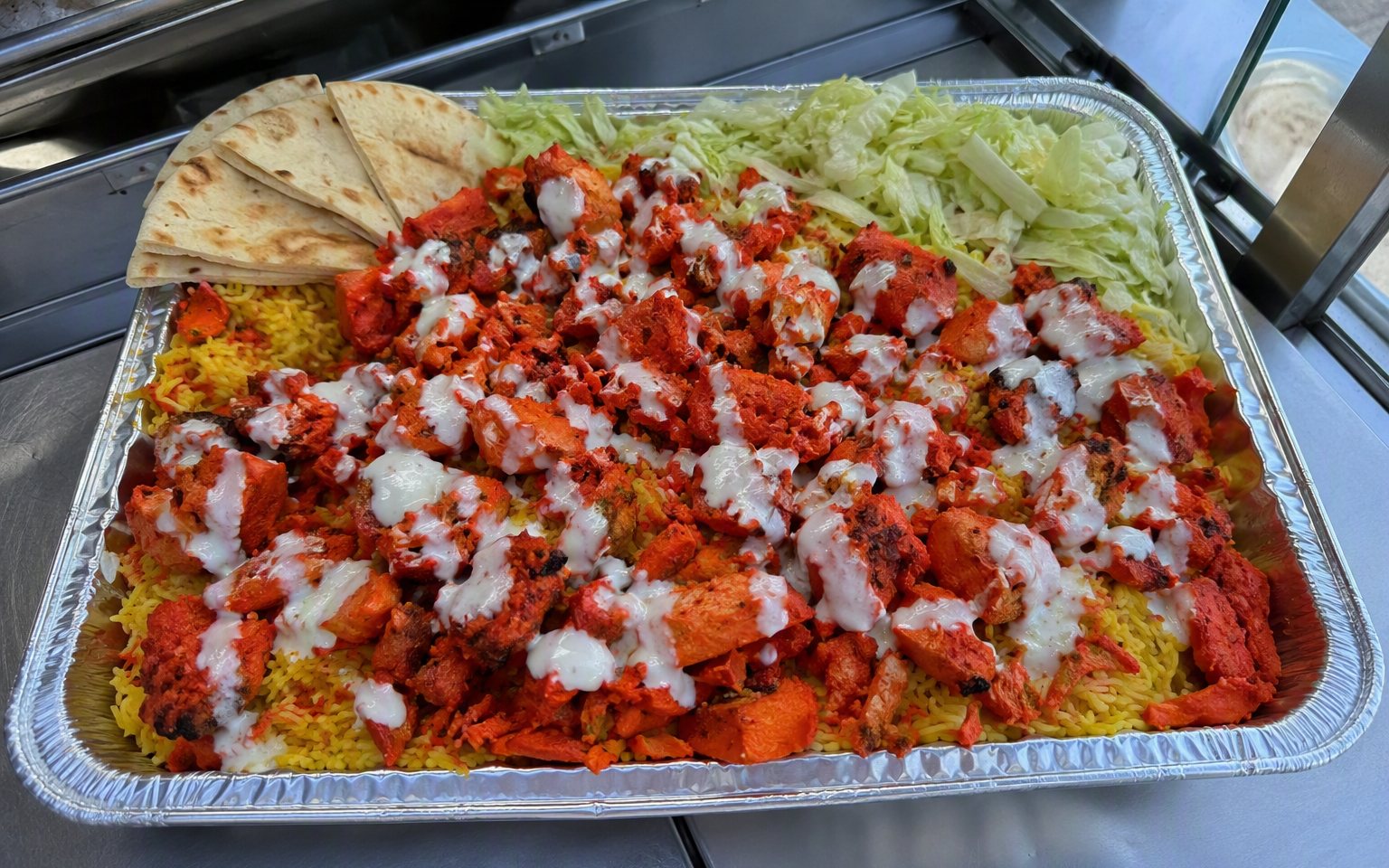 Full catering pan of chicken over rice, salad, pita and white sauce