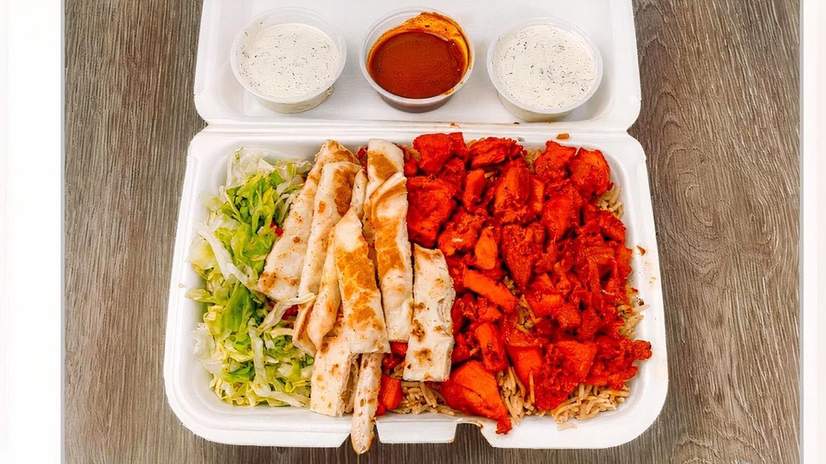 Chicken over rice platter with lettuce, grilled pita strips, white sauce and hot sauce